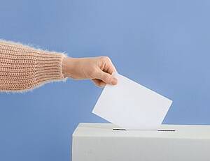 Jemand steckt einen Wahlzettel in eine Wahlurne. 
