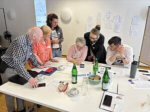 Eine Gruppe Digitallots*innen schaut gemeinsam auf ein Handy. 