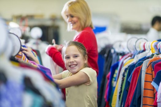 Ein M&auml;dchen st&ouml;bert auf einer Kleiderb&ouml;rse und l&auml;chelt in die Kamera.