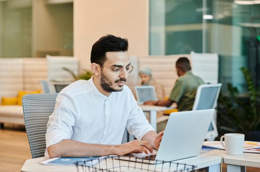 Ein Mann sitzt an einem Schreibtisch.
Er tippt auf einem Laptop.